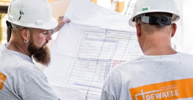 Twee werfmedewerkers van Dewaele bestuderen een bouwplan op de werf.