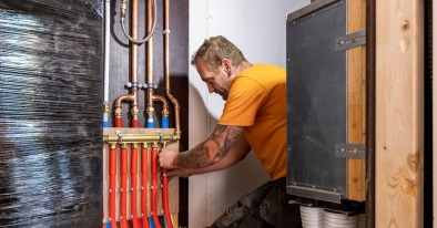 Installateur sluit buizen aan op de verwarmingscollector in een houtskeletbouwwoning.