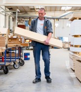 Schrijnwerker draagt houten paneel in werkplaats.