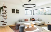 Coin salon moderne avec canapé d’angle et grandes fenêtres dans une maison témoin.