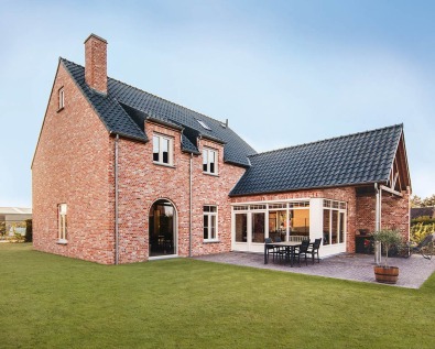 Houtskeletwoning in landelijke stijl met rode bakstenen gevel.